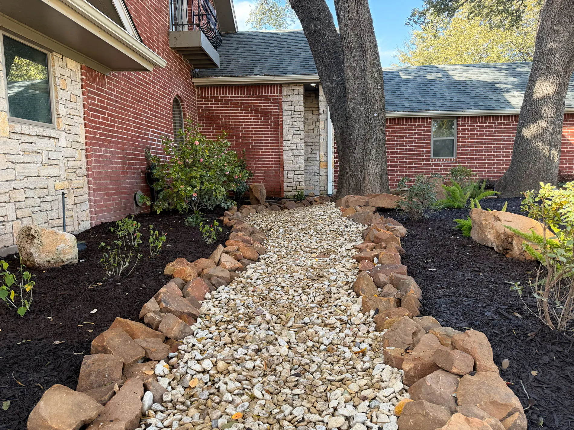 Finished stone walkway with defined landscape beds, rock edging, and planting