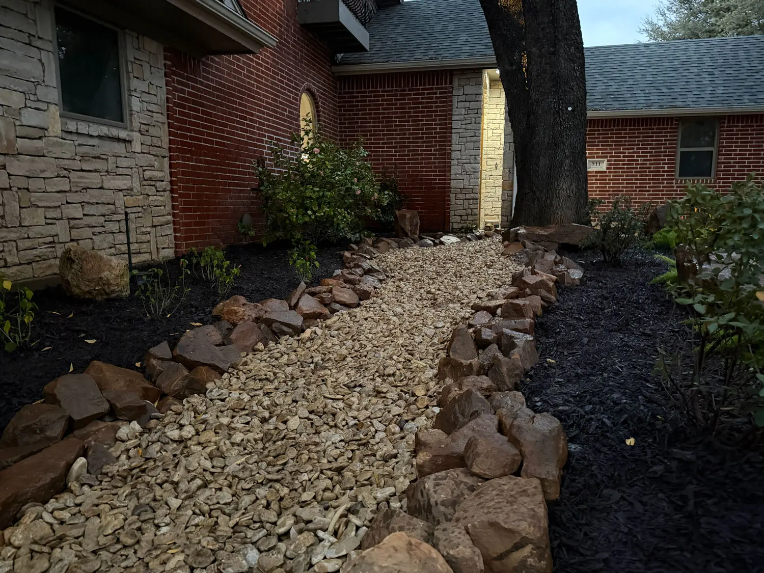 Finished residential landscaping with a rock-lined drainage bed, dark mulch, and foundation planting