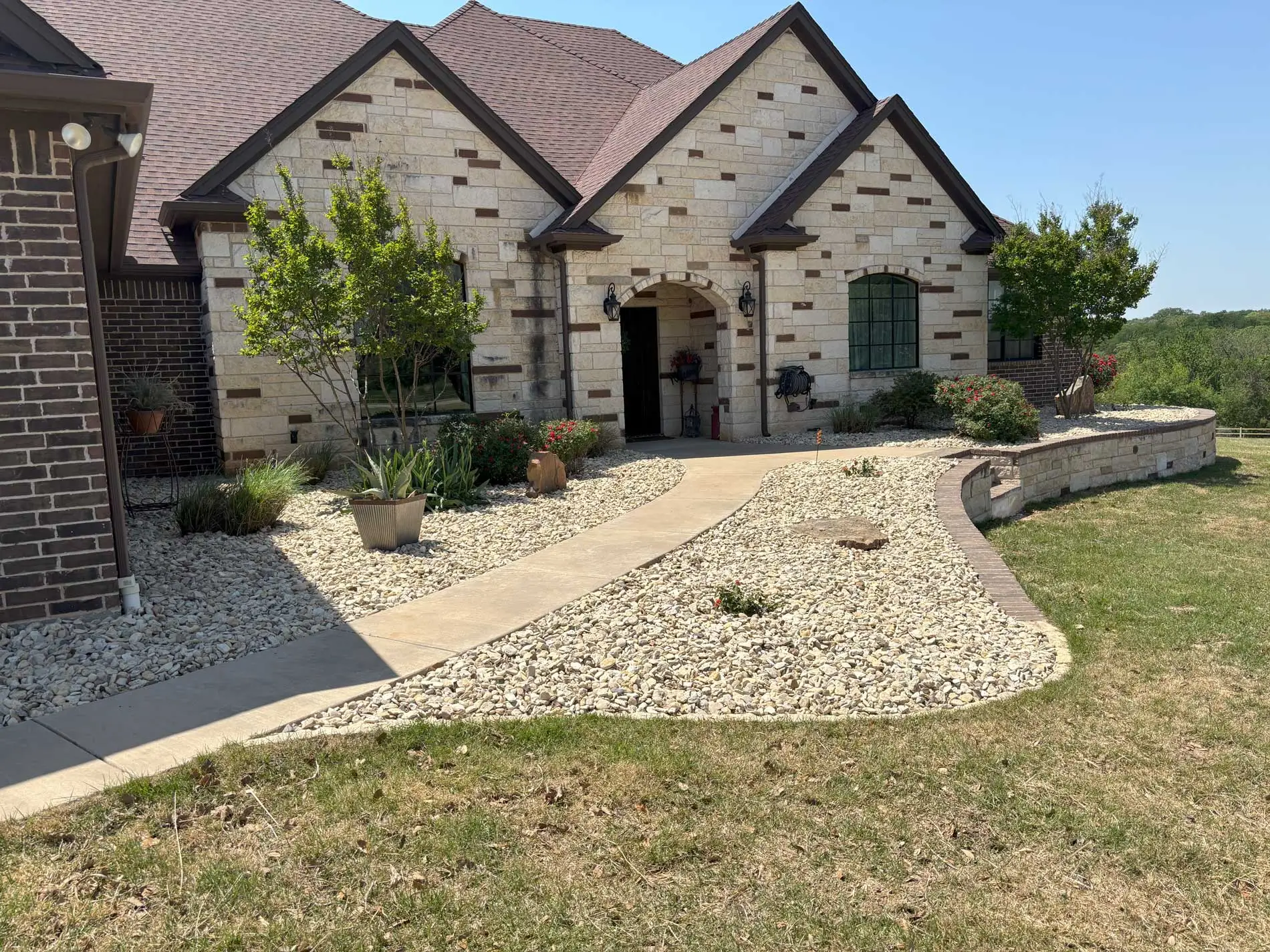 Finished landscaping at a Granbury home with stone beds, planting, lawn, and a curved walkway
