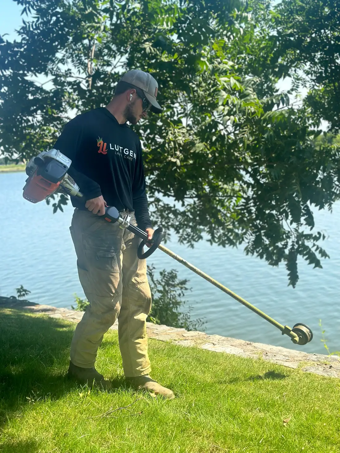Lutgen crew member trimming along a waterfront lawn edge